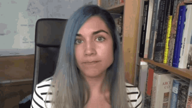 a woman with blue hair is sitting in front of a bookshelf with a book called abc co. on it