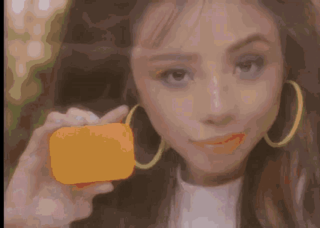 a woman wearing hoop earrings is holding a small yellow object