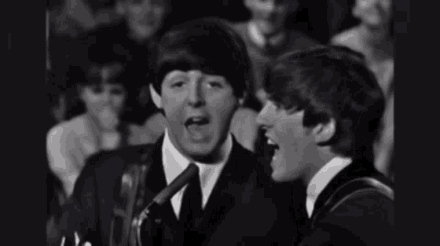 two men singing into microphones with a crowd behind them
