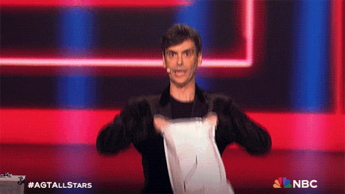 a man is holding a piece of paper on a stage with a nbc logo in the corner