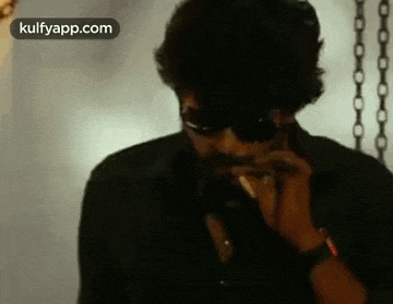 a man wearing sunglasses is smoking a cigarette and talking on a cell phone .