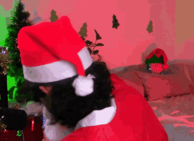 a person wearing a santa hat is sitting on a couch next to a christmas tree