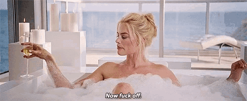 a woman is taking a bath in a bathtub while holding a glass of wine .