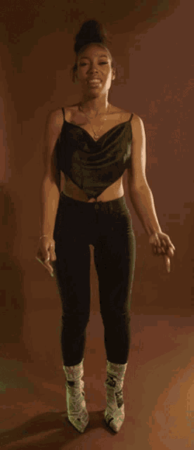 a woman wearing a black top and black pants is standing in front of a brown background