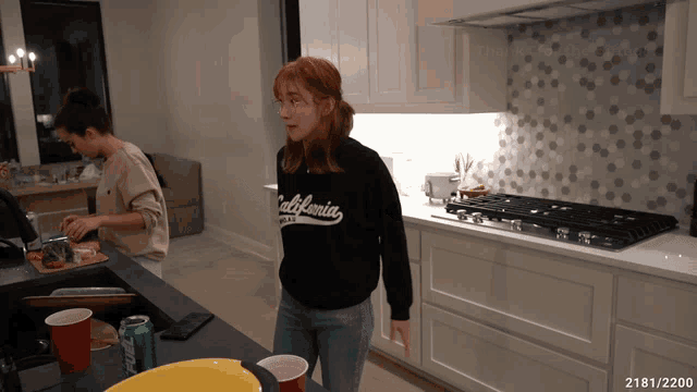 a woman wearing a california sweatshirt is standing in a kitchen