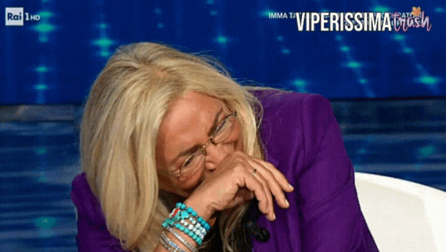 a woman wearing glasses and a purple jacket is laughing on a tv show