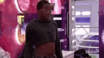 a man in a crop top is standing in front of a vending machine with a global logo on it .