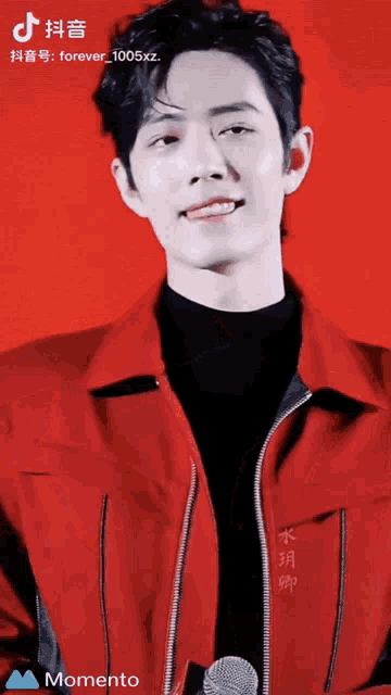 a man wearing a red jacket and a black shirt is standing in front of a red background and a momento icon