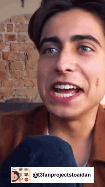 a close up of a young man 's face with a brick wall behind him .