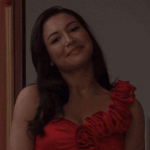 a woman wearing a red dress with ruffles on the shoulder