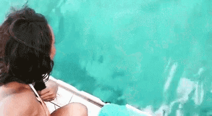 a woman in a bikini is sitting on a boat in the ocean looking at the water .