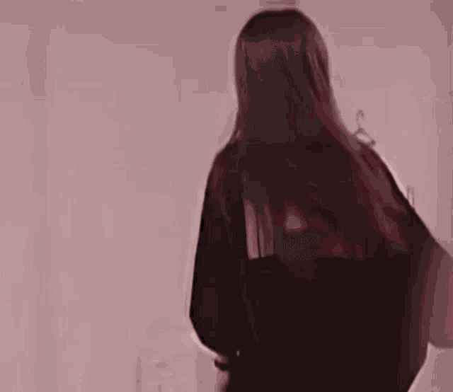 a young woman with long hair is standing in front of a pink wall and smiling .