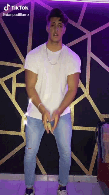 a man in a white shirt and blue jeans is standing in front of a wall with a tiktok watermark on it