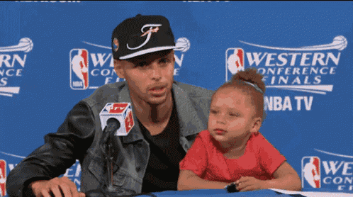 a little girl sits next to a man in front of a blue wall that says western conference finals