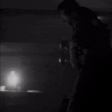 a black and white photo of a man standing in a dark room with a light behind him .