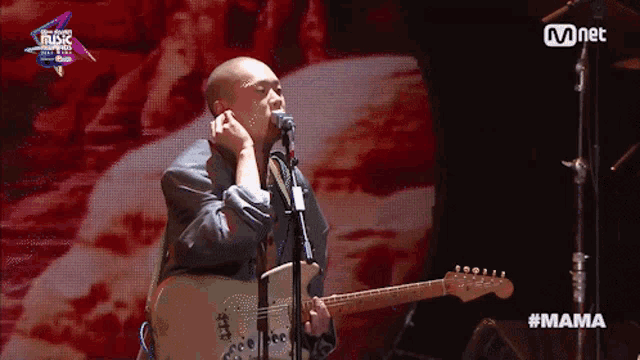 a man singing into a microphone while holding a guitar in front of a mnet logo