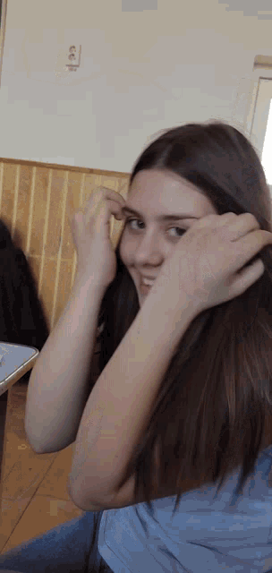 a girl adjusts her eyebrows in front of a wall with an electrical outlet on it
