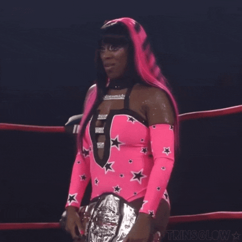 a woman in a pink and black outfit is standing in a ring holding a silver belt