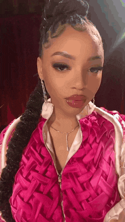 a woman wearing a pink jacket and earrings is taking a picture of herself .