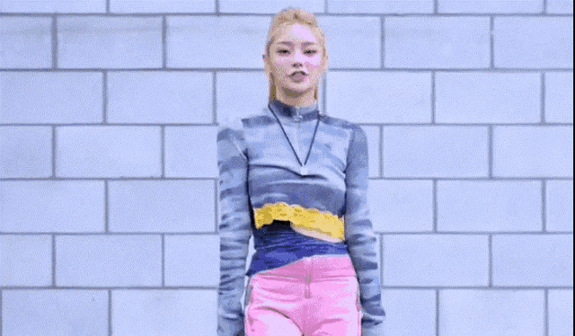 a woman in a blue sweater and pink shorts is standing in front of a brick wall