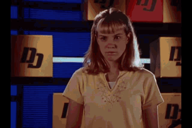 a woman in a yellow shirt is standing in front of a row of yellow boxes with the letter d on them .