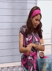 a woman in a pink dress and pink headband is holding a basket and looking at her watch .
