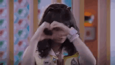 a girl with cat ears is making a heart shape with her hands .
