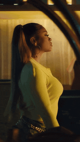 a woman wearing a yellow sweater and hoop earrings looks out of a car window
