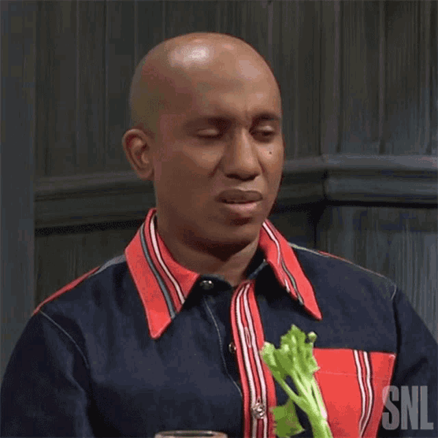 a man in a snl shirt is holding a piece of celery in his hand .