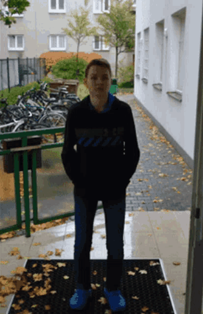 a boy wearing a black sweatshirt that says ' off white ' on it stands in front of a building