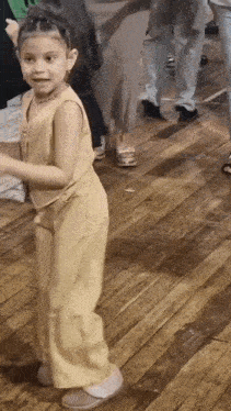 a little girl is dancing on a wooden floor in a room with people .