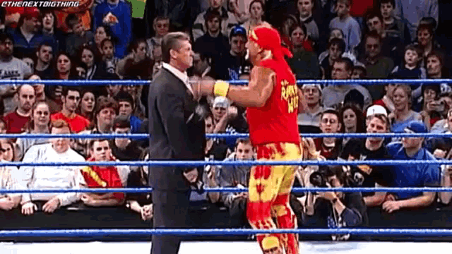 a man in a suit and a wrestler in a red and yellow outfit are standing in a wrestling ring .