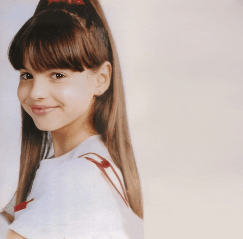 a young girl with long hair and a red bow in her hair smiles for the camera