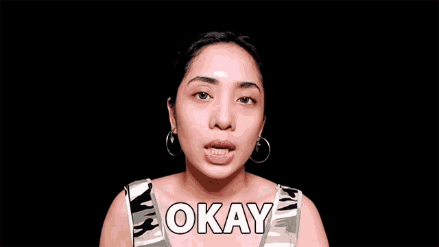 a woman with a surprised look on her face is wearing a tank top that says okay