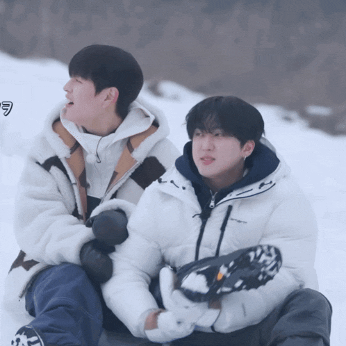 two young men are sitting in the snow and one of them is wearing a jacket that says carhartt on it