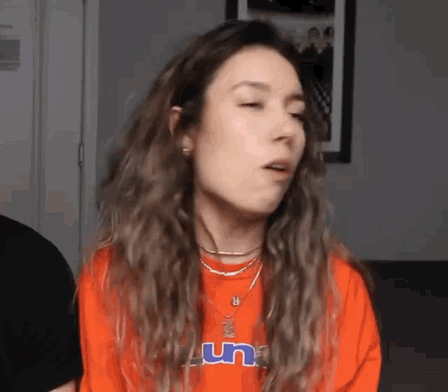 a woman wearing a red shirt and necklaces is making a face .