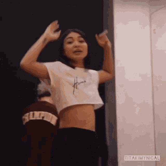 a woman in a white crop top is dancing with her hands in the air .