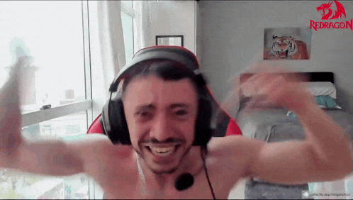 a shirtless man wearing headphones and a red dragon logo on the wall behind him