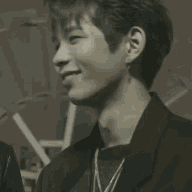 a black and white photo of a young man wearing a black jacket and earrings .