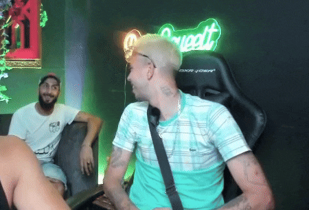 a man in a green shirt is sitting in front of a neon sign that says ' sweet '