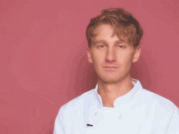 a man wearing a white chef 's coat stands in front of a pink background