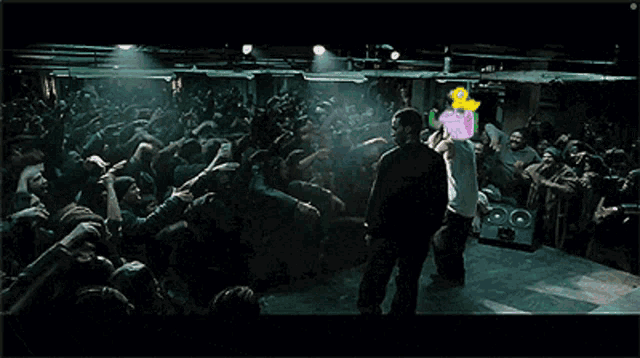 a man stands on a stage in front of a crowd of people with a cartoon character on his head