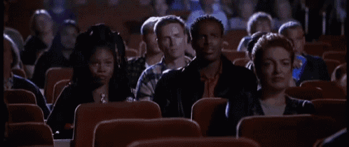 an elderly woman is sitting in a theater watching a movie and making a funny face .