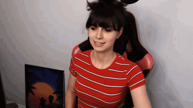 a woman wearing a red and white striped shirt is sitting in a pink chair