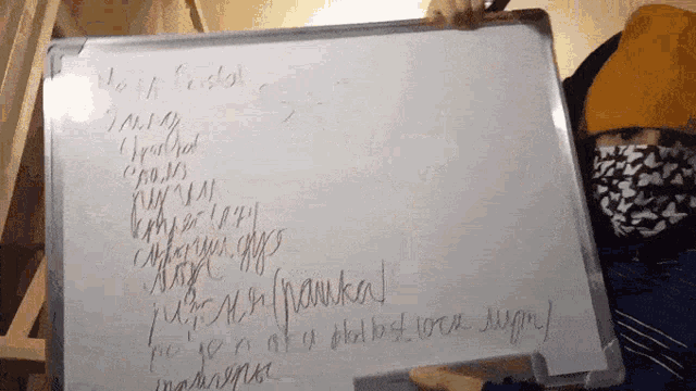 a person wearing a face mask holds up a whiteboard with russian writing on it