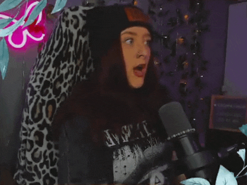 a woman wearing a black hat and a t-shirt that says ave it stands in front of a microphone