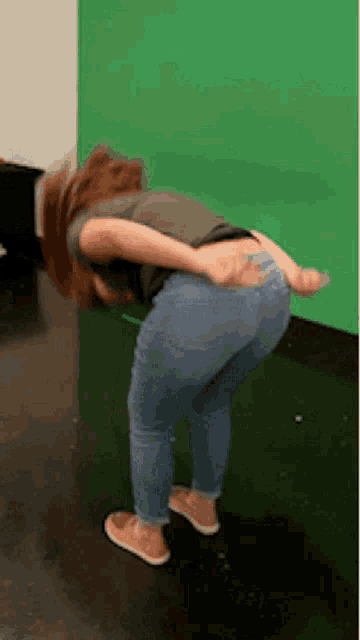 a woman in jeans is bending over on the floor in front of a green screen .