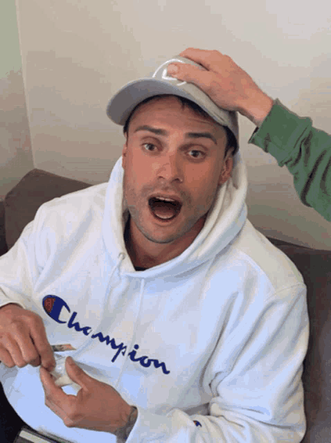 a man is wearing a white champion hoodie and a hat