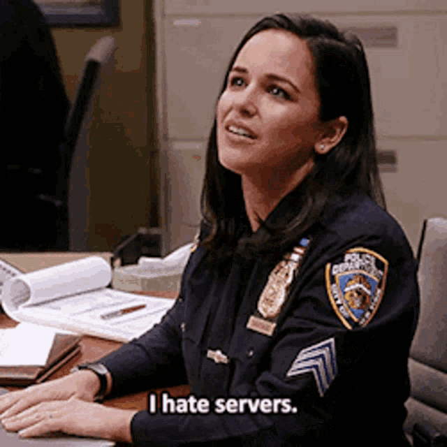 a woman in a police uniform is sitting at a desk and saying i hate servers .