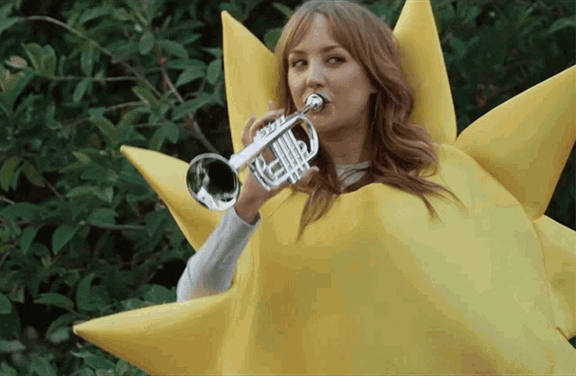 a woman wearing a yellow sun costume is playing a trumpet